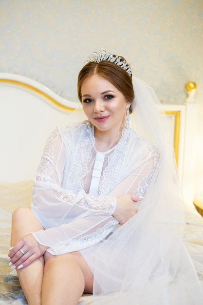 The bride in a white coat on the bed in a wedding morning