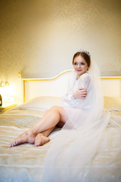 The bride in a white coat on the bed in a wedding morning