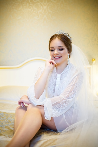 The bride in a white coat on the bed in a wedding morning