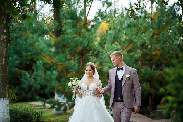 Bride in white dress and groom in costume cuddle and walk in the park