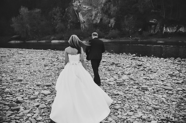 Bride in a white dress and groom go to the river stones