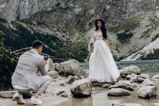 The bride in a white dress and groom standing near the river and hugging and sunshine