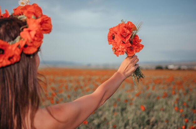 ポピーの花の花束を保持している白いドレスの花嫁は、背景に暖かい日没の時間を暖かく