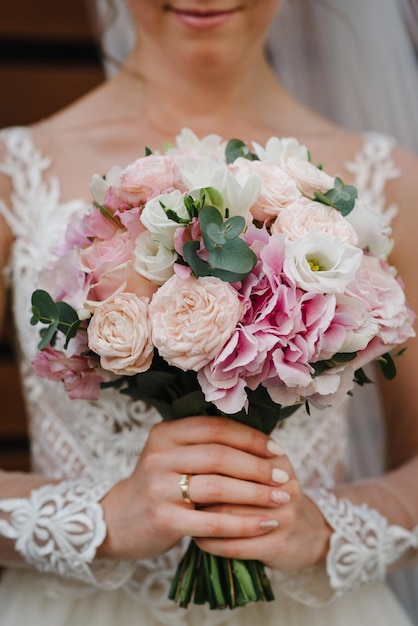 The bride in a white dress holds a wedding bouquet The bouquet with white pink purple roses eucalyptus leaves On the bride's hand is a wedding ring