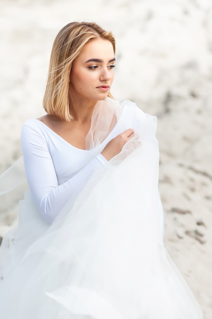Bride in white dress outdoor on the sand and blue sky background