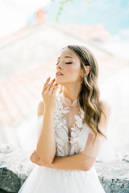 Bride in a white dress touches her chin with her fingers portrait