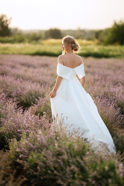 La sposa in abito bianco cammina sul campo di lavanda