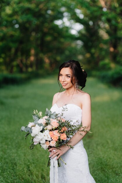 Bride in a white dress with a large spring bouquet in a green forest