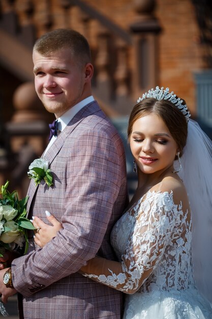 The bride in a white wedding dress and groom in a suit on the\
background of a brick building with large steps