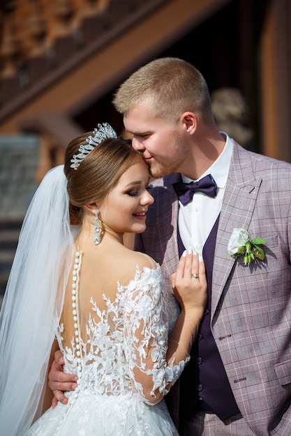 The bride in a white wedding dress and groom in a suit on the\
background of a brick building with large steps