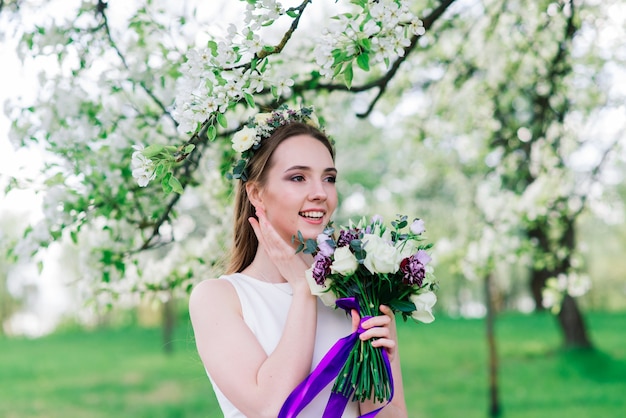 The bride in white wedding dress is holding a bouquet in green park