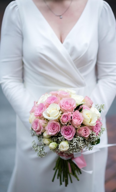 The bride in a white wedding dress is holding a bouquet of\
white flowers peonies roses wedding bride and groom delicate\
welcome bouquet beautiful decoration of weddings with leaves