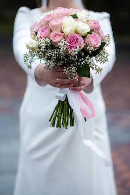 The bride in a white wedding dress is holding a bouquet of white flowers peonies roses Wedding Bride and groom Delicate welcome bouquet Beautiful decoration of weddings with leaves