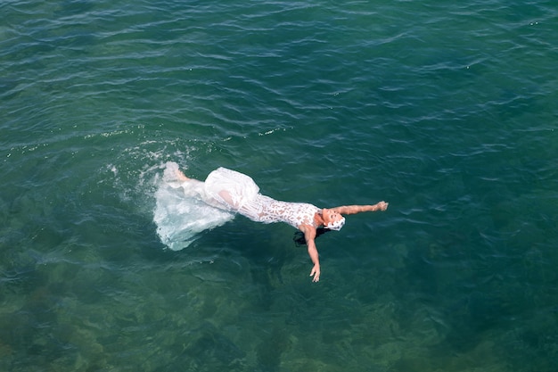 Foto il vestito da sposa bianco della sposa pone l'acqua di mare. abito da sposa bagnato caldo giorno di sole. la sposa felice gode del fondo dell'oceano di vacanze estive. luna di miele in località di mare. matrimonio all'estero. cerimonia di nozze in riva al mare.