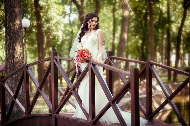 The bride in a white wedding dress stands against the backdrop of an artificial waterfall in a city park