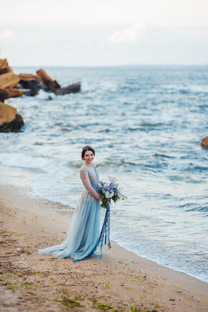 Bride with a bouquet of flowers on the beach near the water