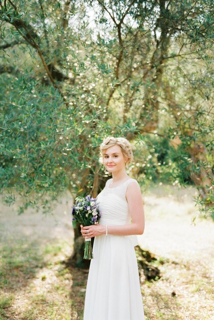 Bride with a bouquet of flowers stands under an olive tree