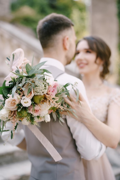 Bride with a bouquet hugs groom on the stone steps portrait