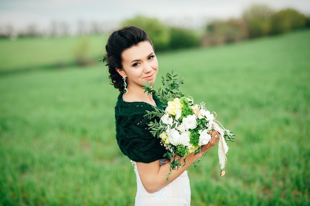 Bride with a bouquet in an ivory dress and a knitted shawl on a green field