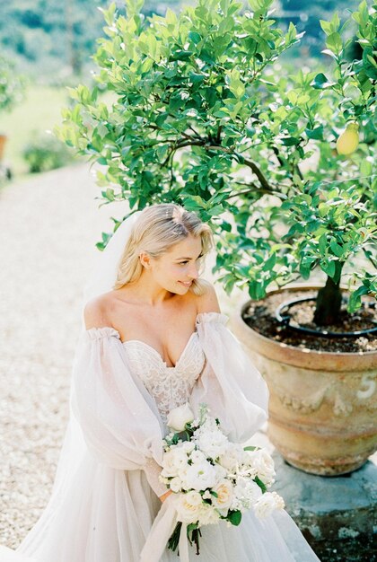 Bride with a bouquet of roses near a tree in a tub in the garden