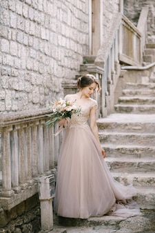 La sposa con un bouquet si trova sui gradini di pietra vicino al recinto