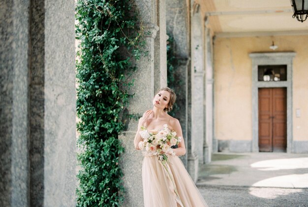 La sposa con un bouquet si erge sul terrazzo di un'antica villa vicino alla colonna