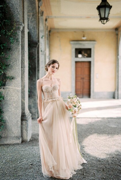 Bride with a bouquet stands on a terrace with arches of an old villa