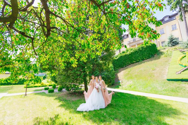 Bride with bridesmaids in the park on their wedding day holding a beautiful bouquet with peonies in the background a greenery garden and a palace