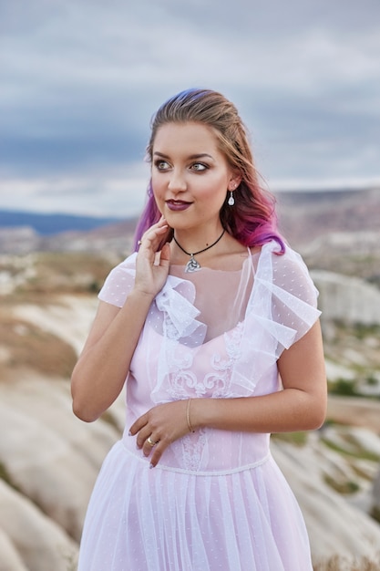 Bride with creative hair coloring looks into the distance in nature. Portrait of a woman with brightly colored hair standing in the mountains of Cappadocia in Turkey.