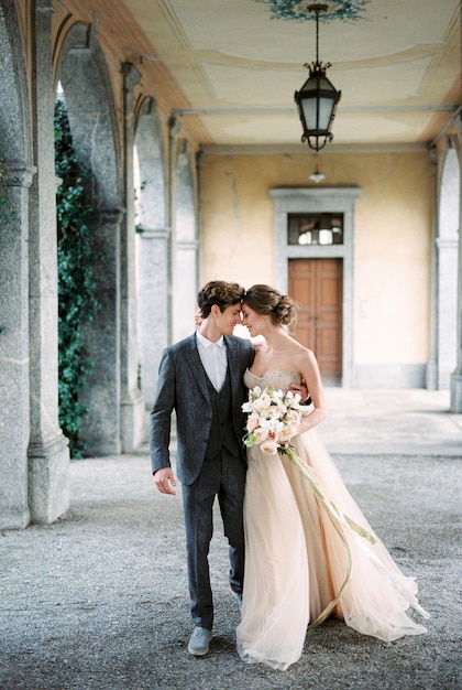 Bride with flowers hugs groom on the terrace with arches in the garden