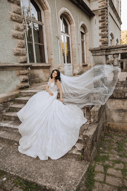 bride with long curly hair in white dress with long train near castle in beautiful flowers Beautiful