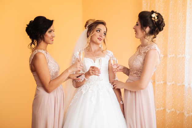 Bride with merry girlfriends at the wedding drink champagne from glasses