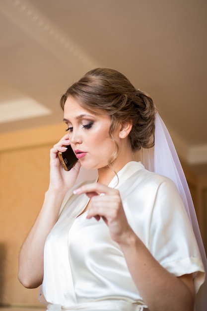 The bride with a veil on her head talking on the phone in hotel room