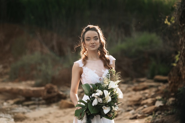 Bride with a wedding bouquet on the shore of the black sea in the sunset light