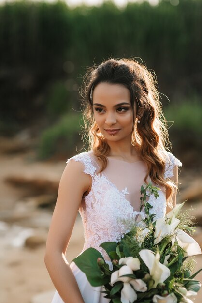 Bride with a wedding bouquet on the shore of the black sea in the sunset light