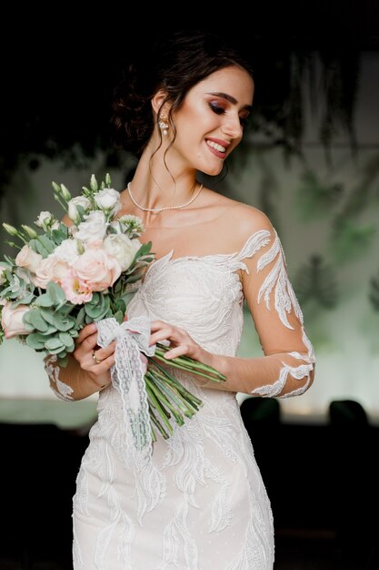 Bride with wedding bouquet smiles. Girl in wedding dress in luxury restaurant.