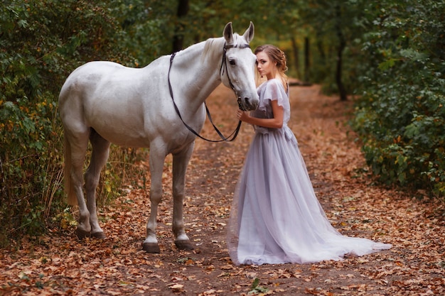 bride with a white horse walks in the summer forest. Background blurred, artistic effect.