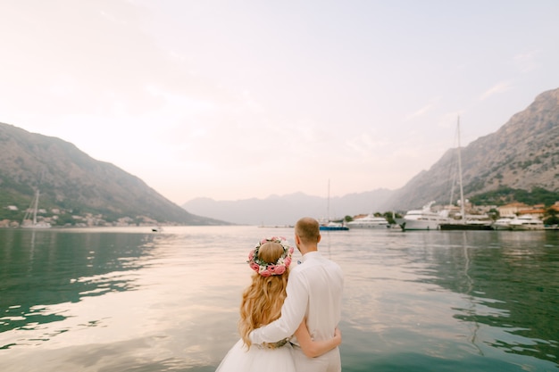 The bride in a wreath and groom hug on the pier near the old town of kotor in the bay of kotor