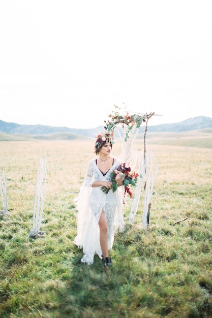 Bride in a wreath walks past a wedding arch on a green lawn