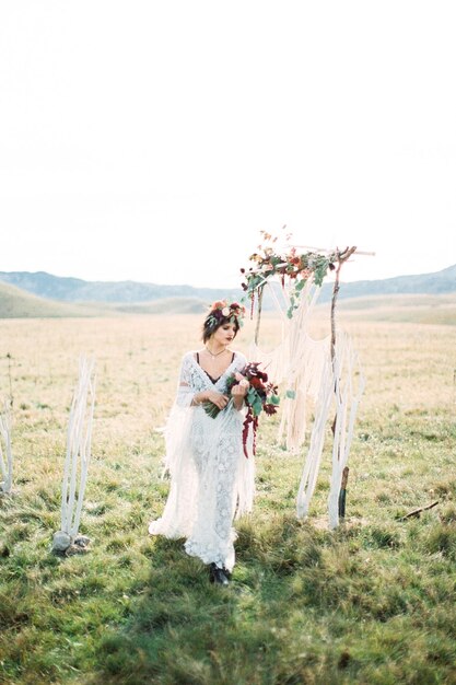 Bride in a wreath with a bouquet walks past the wedding arch