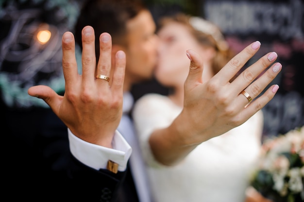 Bridegroom and bride kissing and showing wedding rings on their fingers