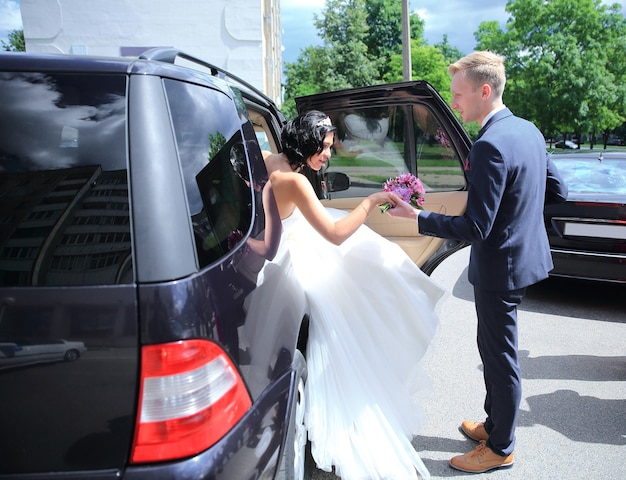 Bridegroom helps the bride out of the Bridal car