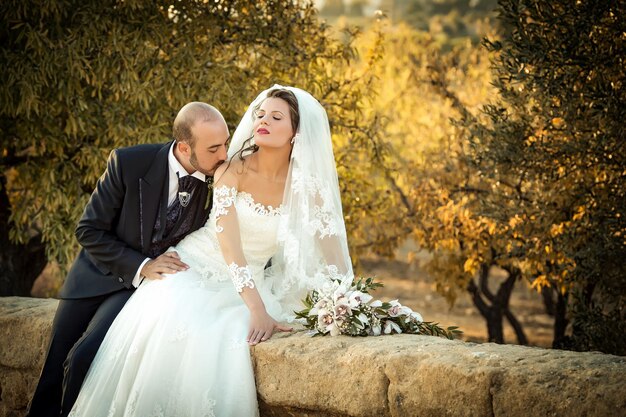 Foto lo sposo bacia la sposa sulla spalla al muro di supporto durante il tramonto