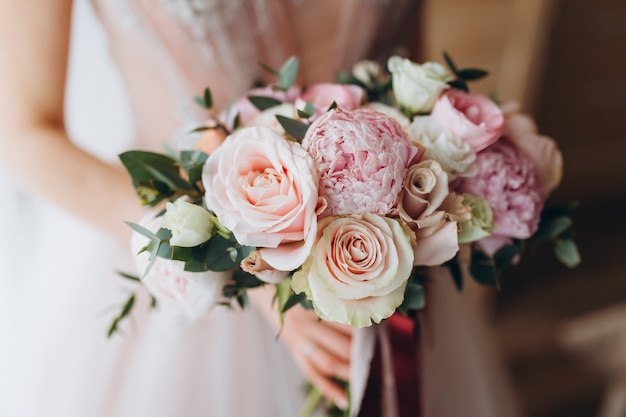 Brides wedding bouquet with peonies, freesia and other flowers in women's hands. Light and lilac spring color. Morning in room