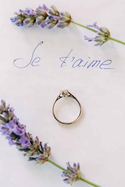 The brides wedding ring with a gemstone on a white sheet with the inscription je taime and lavender