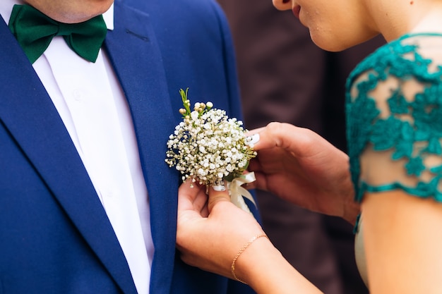 Bridesmaid fixes a small bouquet on the jacket of the groom witness