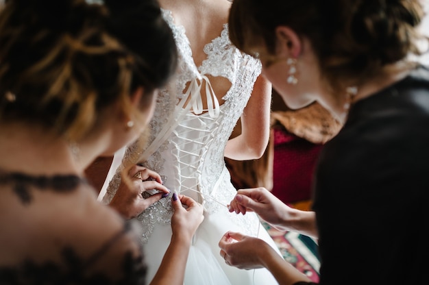 写真 花嫁介添人は、花嫁がコルセットを締めてドレスを着るのを手伝い、結婚式の日の朝に花嫁を準備します。