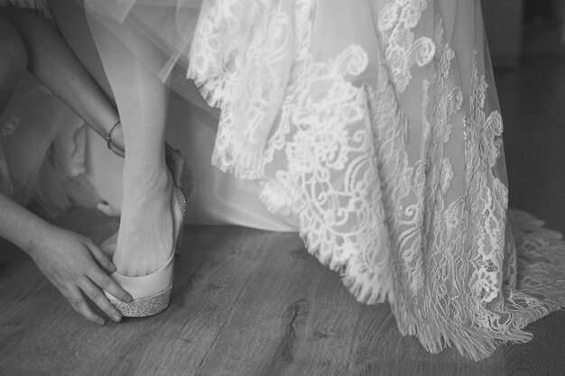 Bridesmaid helping bride to put on elegant shoes Black and white shot