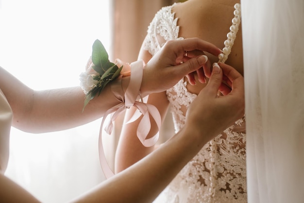 A bridesmaid helps a bride to wearing in wedding day morning close up