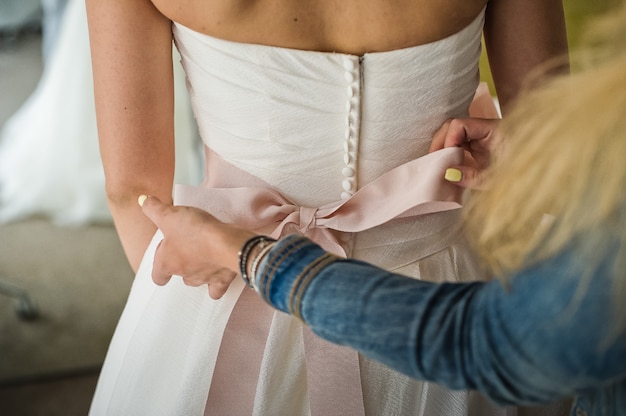 Foto damigella d'onore aiuta a indossare un abito da sposa